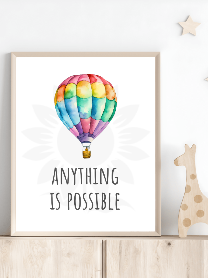 Nursery room decor with framed wall art of a vibrant hot air balloon and the text 'ANYTHING IS POSSIBLE.' The design, from Blossoming Minds, is displayed on a shelf next to a wooden giraffe toy, encouraging positive affirmations and dreaming big for children