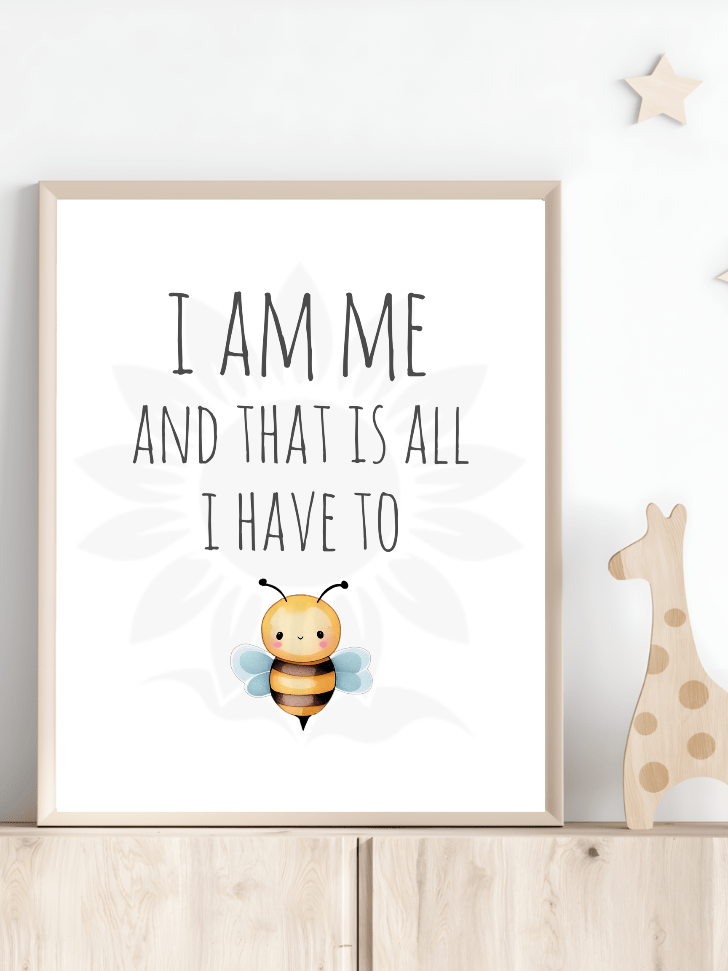 Nursery room decor with framed wall art of a cute, smiling bee and the text 'I AM ME AND THAT IS ALL I HAVE TO BE.' The design, from Blossoming Minds, is displayed on a shelf next to a wooden giraffe toy, encouraging positive affirmations, self-acceptance, and individuality for children.